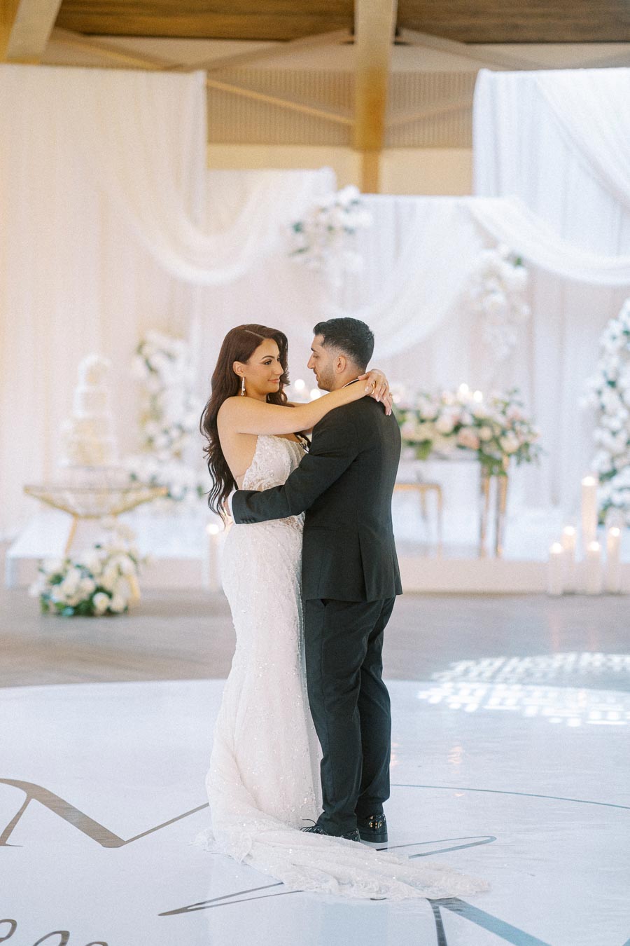 Elegant bride and groom share their first dance at a beautifully decorated wedding venue with white floral arrangements and