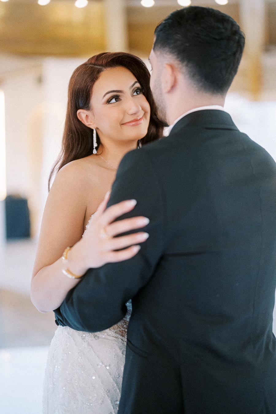 Bride and groom dancing at their wedding, with the bride wearing a white gown and earrings, sharing a joyful and loving