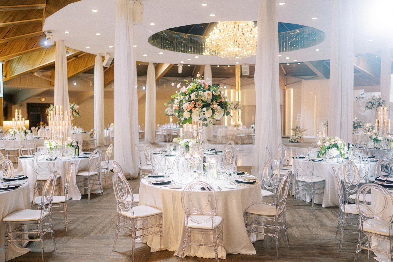 Elegant wedding reception venue with round tables dressed in white linens, decorated with tall floral centerpieces and