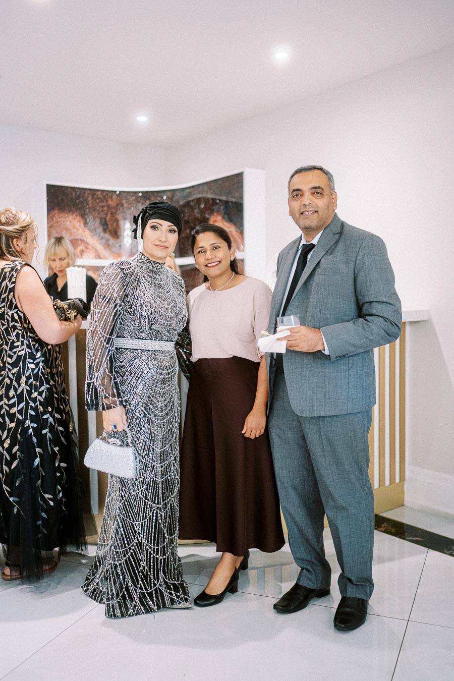 Group of elegantly dressed people posing at a formal event, featuring a woman in a shimmering gown holding a metallic purse,