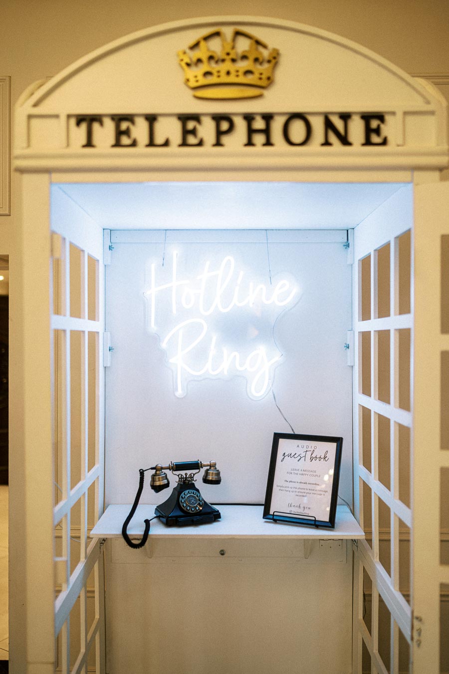 Vintage telephone booth with a neon sign reading Hotline Ring. The booth features an old-fashioned rotary phone and an audio