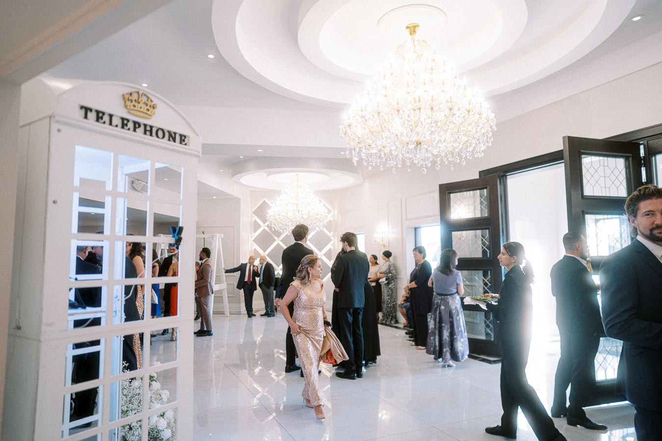 Elegant wedding reception hall with guests socializing under luxurious chandeliers, featuring a classic white telephone