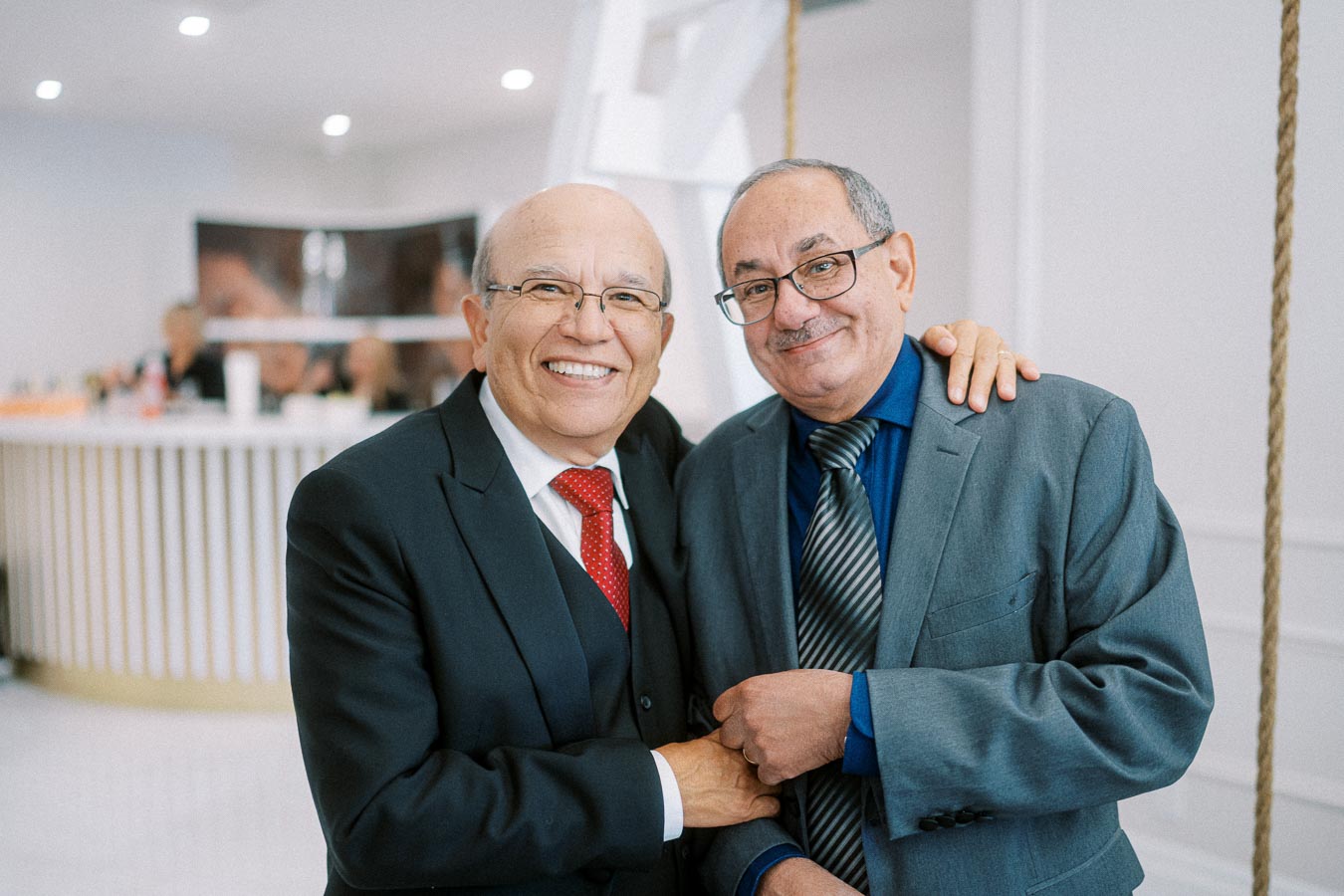Two elderly men in suits smiling warmly, standing together in a bright, modern setting, exuding a sense of friendship and