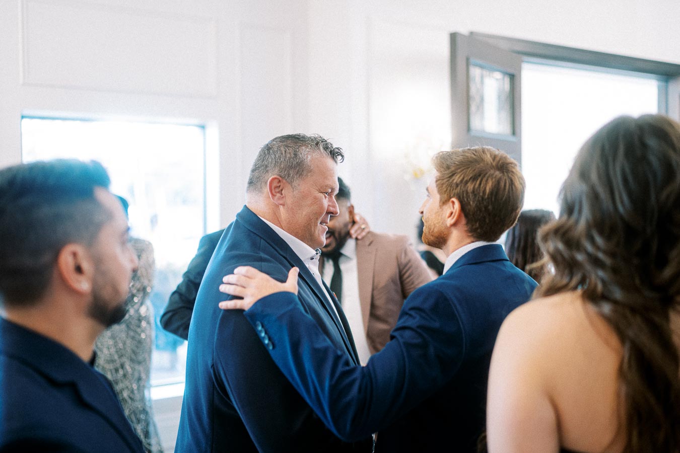 A group of people in formal attire engaged in a friendly conversation at a social event, with one person placing a