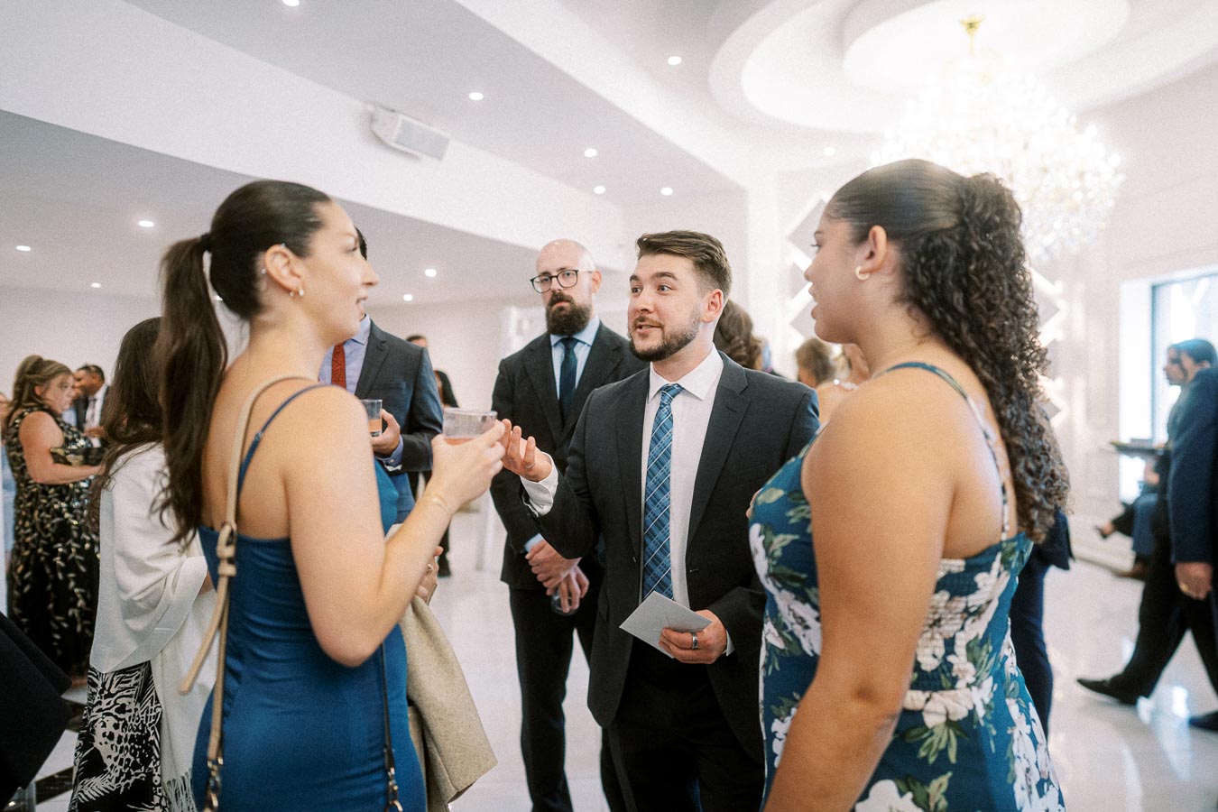 A group of well-dressed individuals engaged in conversation at an elegant social event, featuring modern decor and a large
