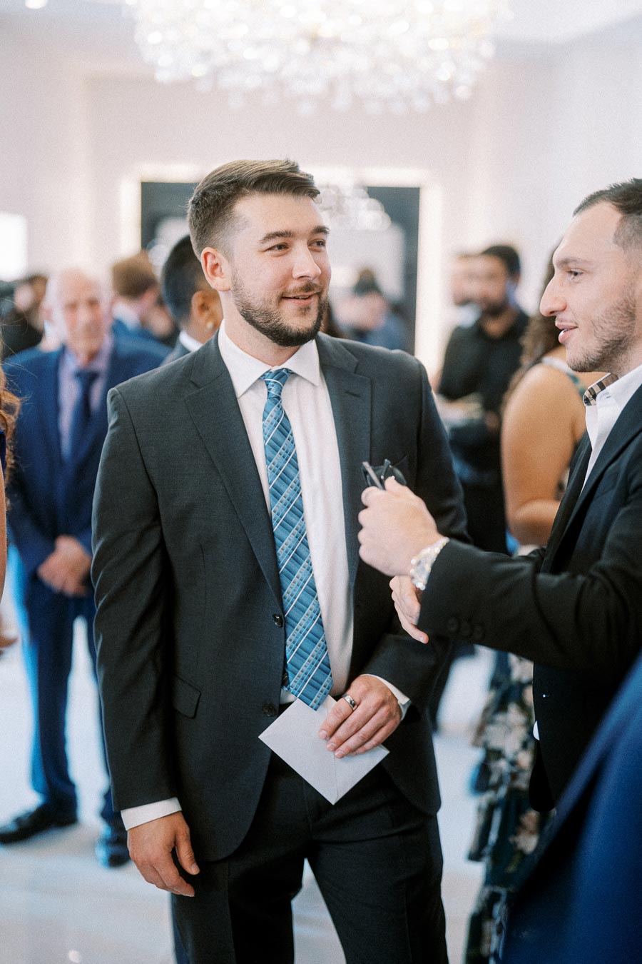 A man in a suit with a blue patterned tie smiling while conversing at a formal event.