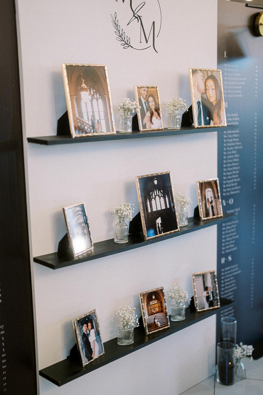 Stylish wedding photo display with elegant framed pictures and delicate white flowers on minimalist black shelves against a