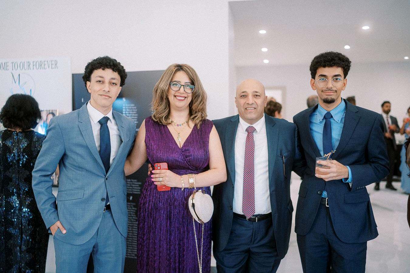 A group of four people dressed in formal attire at an event, with a woman in a purple dress holding a phone and smiling.