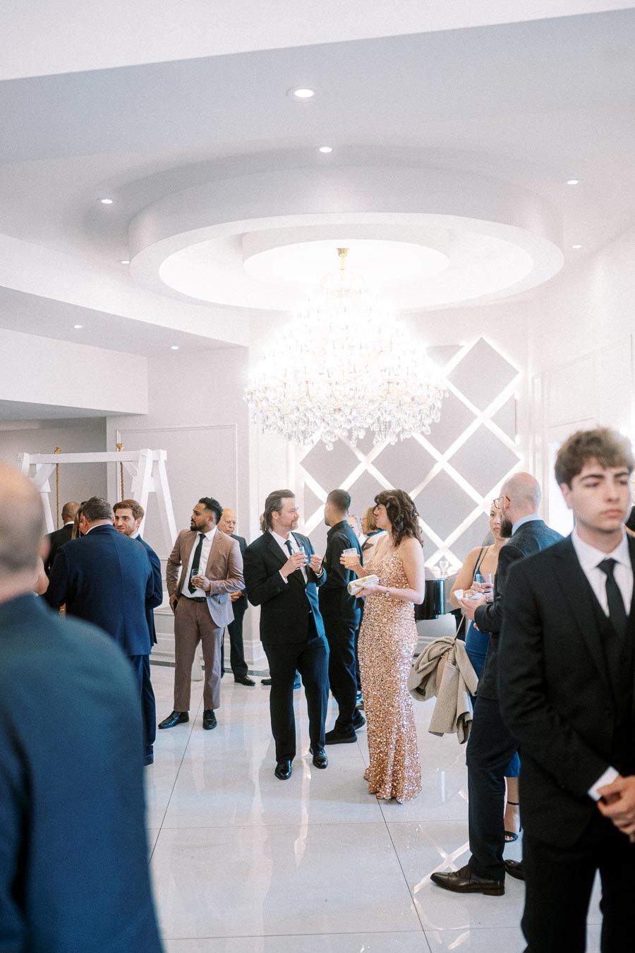 Elegant cocktail party gathering in a luxurious venue with guests in formal attire, featuring a stunning chandelier and