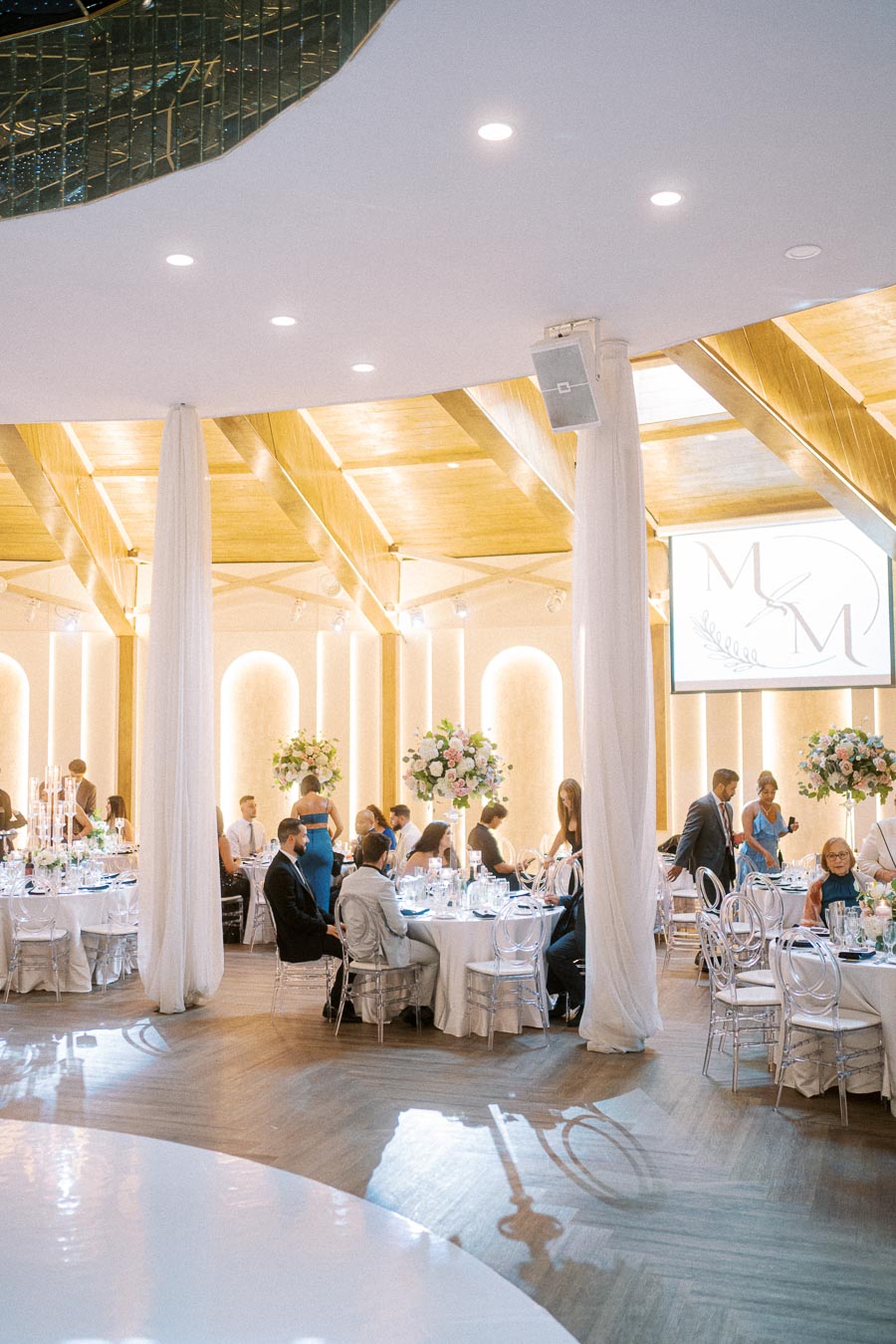 Elegant wedding reception in a beautifully decorated venue with guests seated at round tables adorned with floral