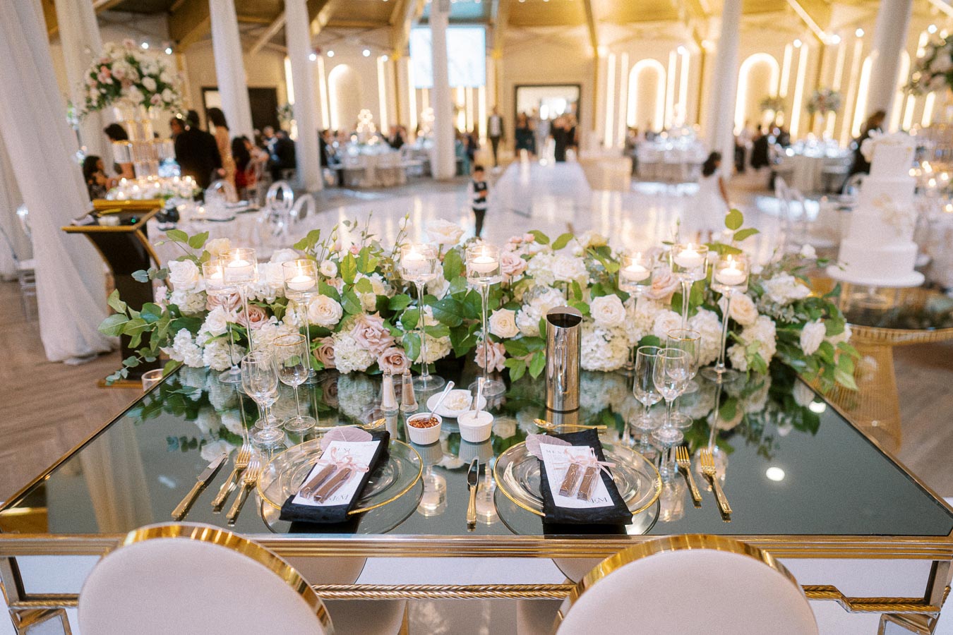 Elegant wedding reception venue with a lavishly decorated sweetheart table featuring a floral centerpiece of white and blush