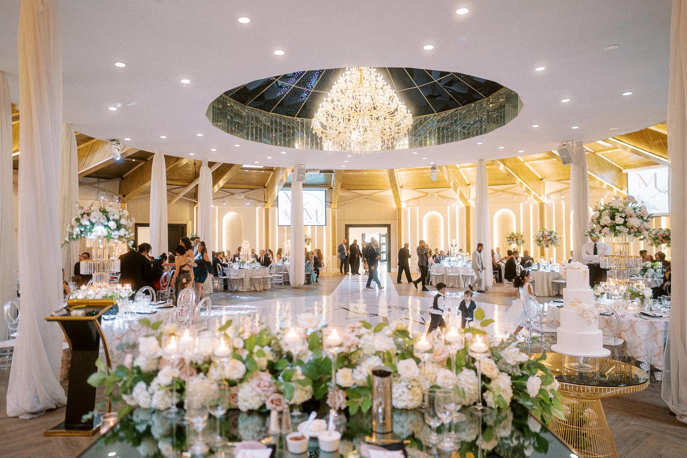 Luxurious wedding reception venue with elegant floral arrangements and chandeliers, featuring round tables set for guests