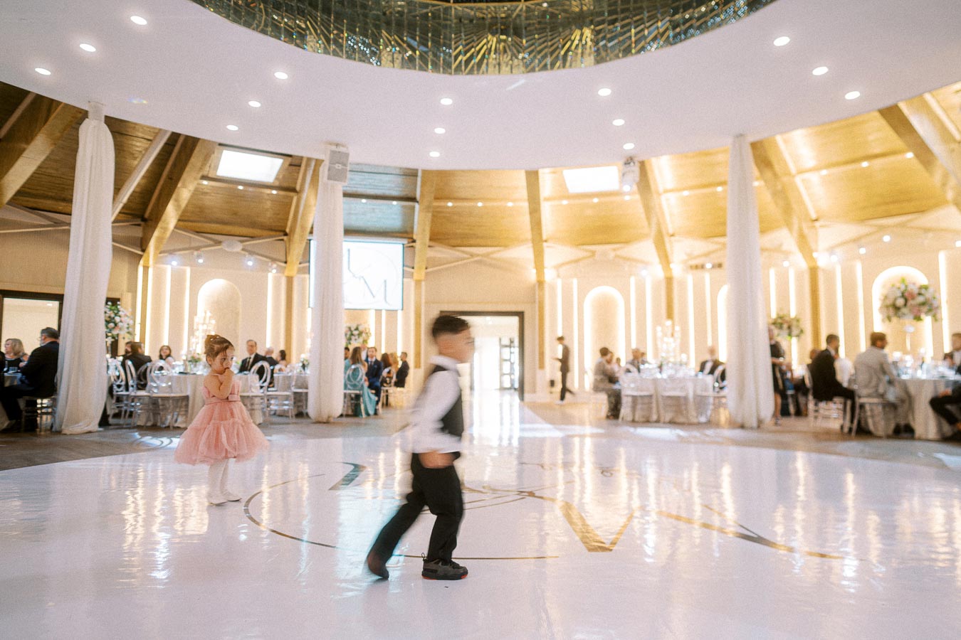 A beautifully decorated wedding reception venue with elegant round tables set for guests and soft ambient lighting. A young