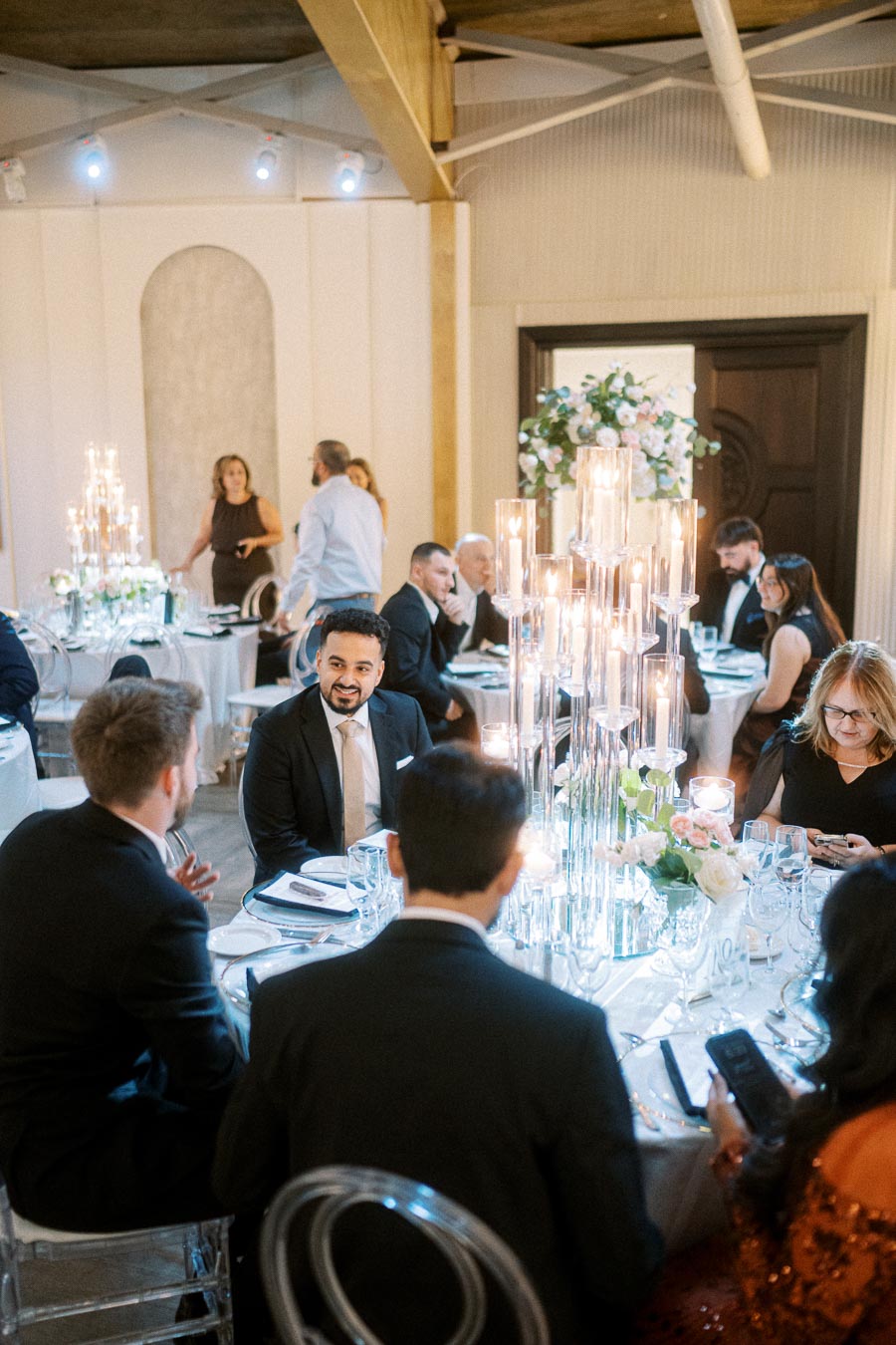 Elegant dinner event with guests in formal attire seated at a beautifully decorated table featuring tall candle centerpieces