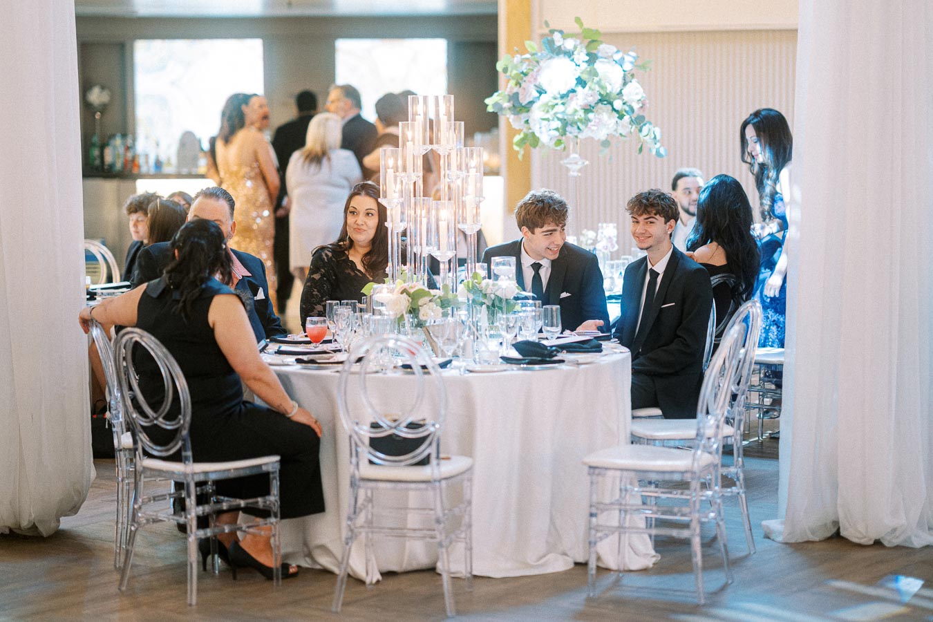 Guests sitting at an elegantly decorated table during a formal event, surrounded by floral centerpieces and candlelight,
