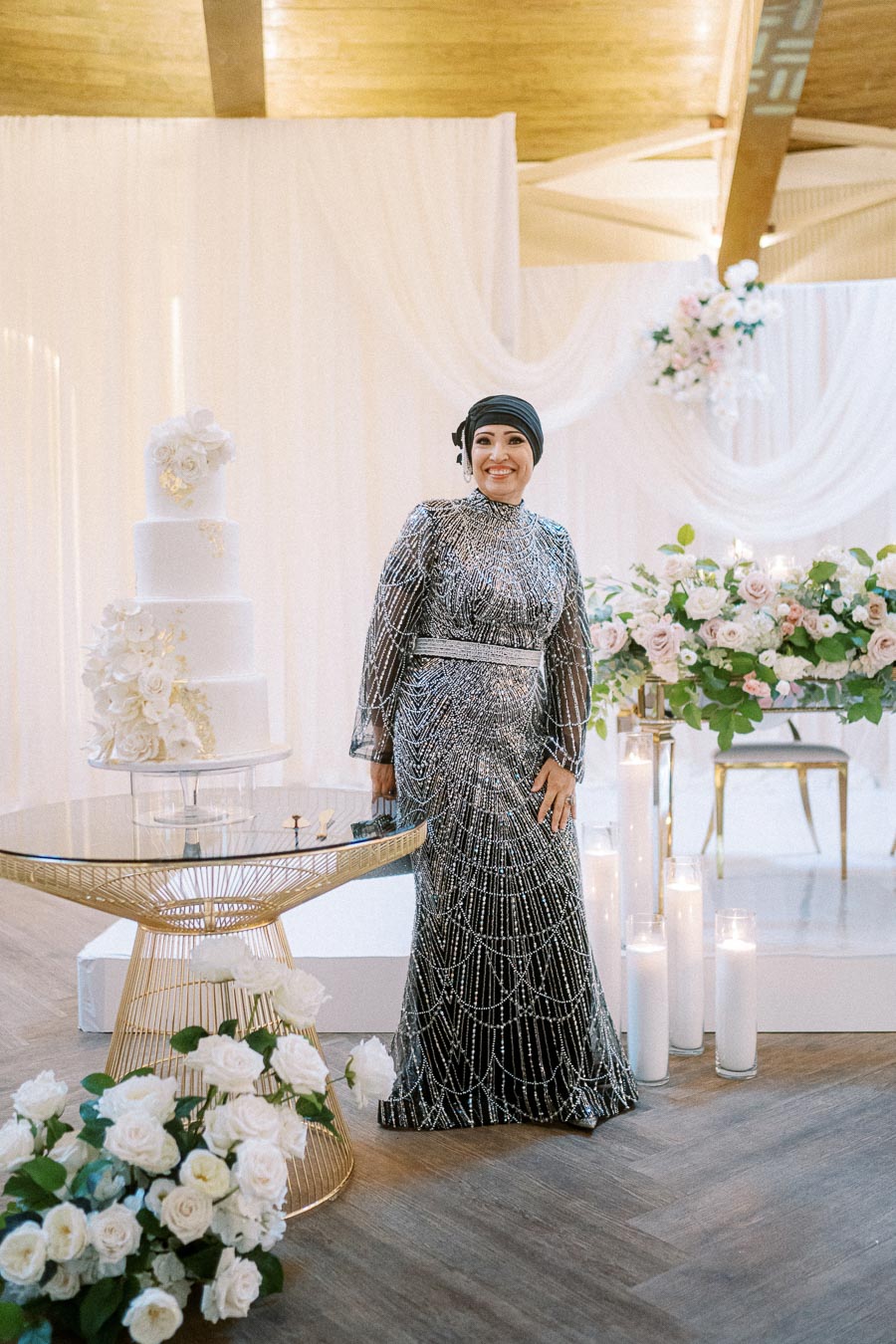 Wedding celebration with an elegantly dressed woman in a sparkling gown standing beside a multi-tiered white wedding cake