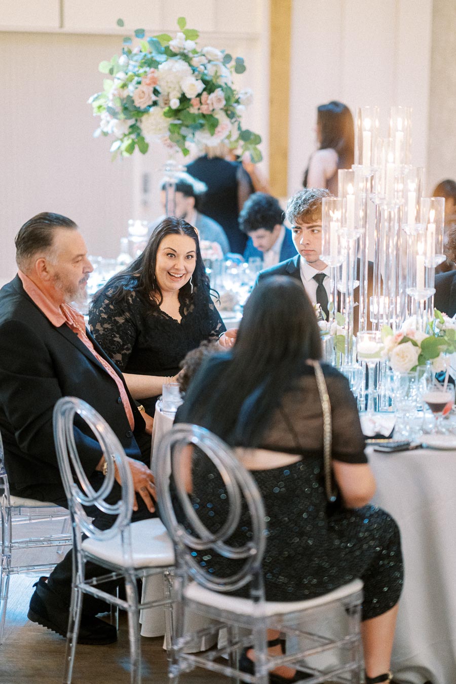 Group of elegantly dressed people enjoying a formal dinner at an event, surrounded by floral arrangements and candlelit