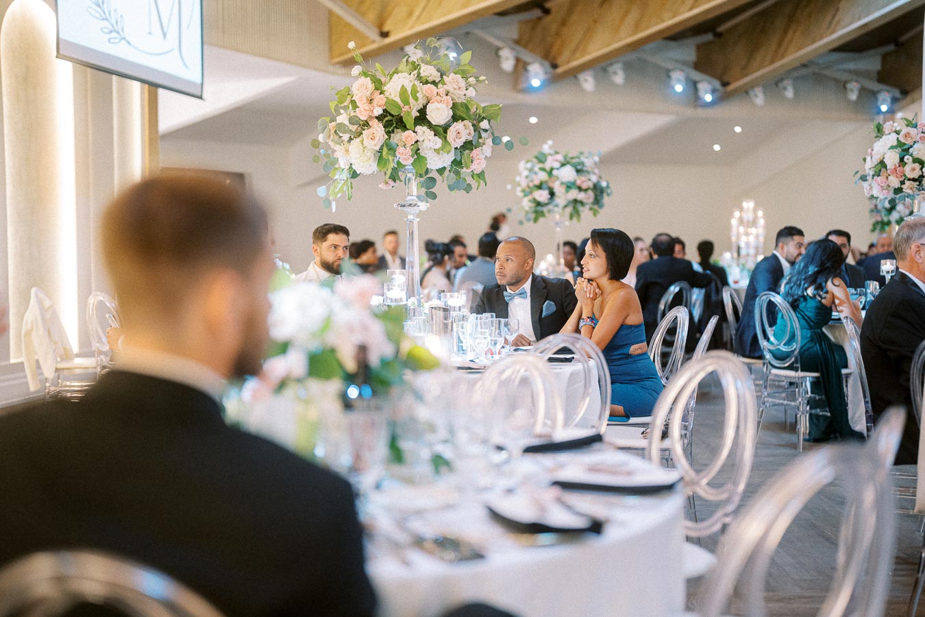 Elegant wedding reception with guests seated at tables adorned with floral centerpieces and crystal-clear plates, creating a