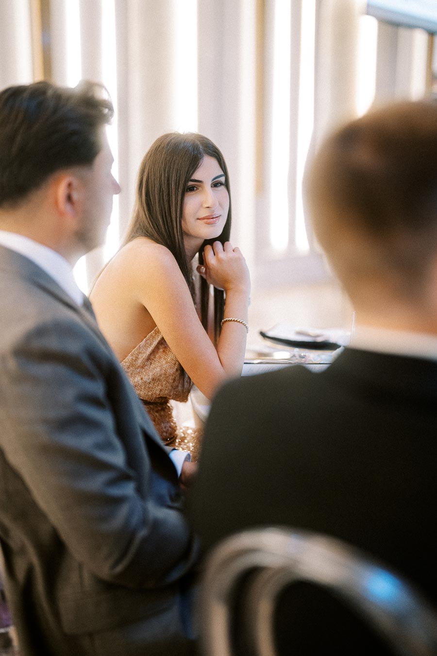 Elegant woman in a formal setting attending an event, surrounded by people in suits.