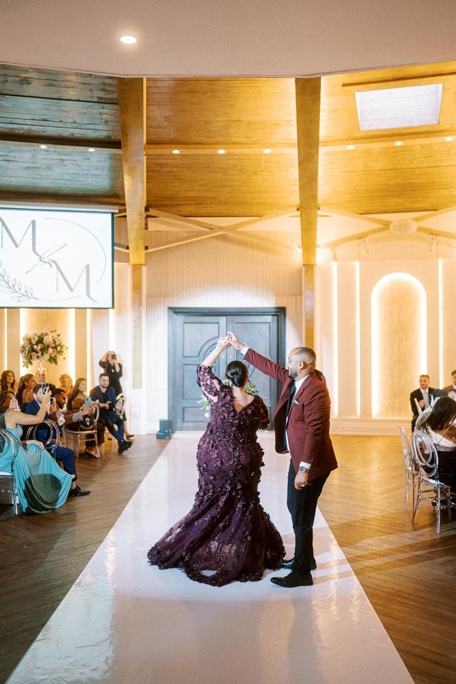 A couple dancing elegantly on a polished dance floor during a wedding reception at a stylish venue, surrounded by guests
