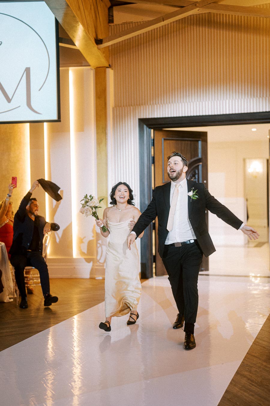 A joyful couple enters a beautifully decorated wedding venue, the bride in an elegant white gown holding a bouquet and the