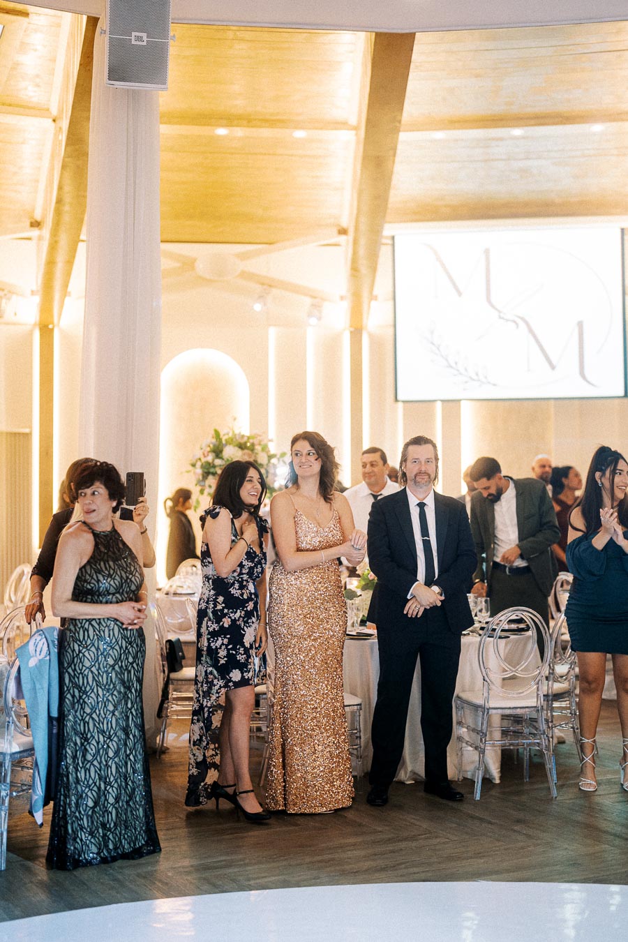 Guests elegantly dressed in formal attire enjoy a wedding reception in a beautifully decorated venue with floral