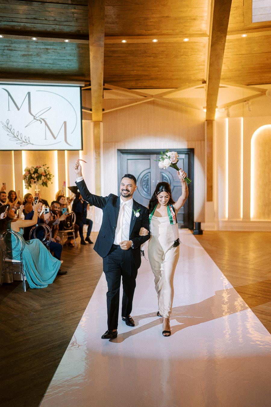 Bride and groom joyfully walking down the aisle, celebrating their wedding day at a beautifully decorated indoor venue,