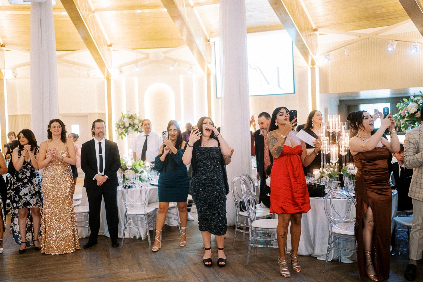Guests joyfully celebrating at a wedding reception, capturing the moment with smartphones in a beautifully decorated venue