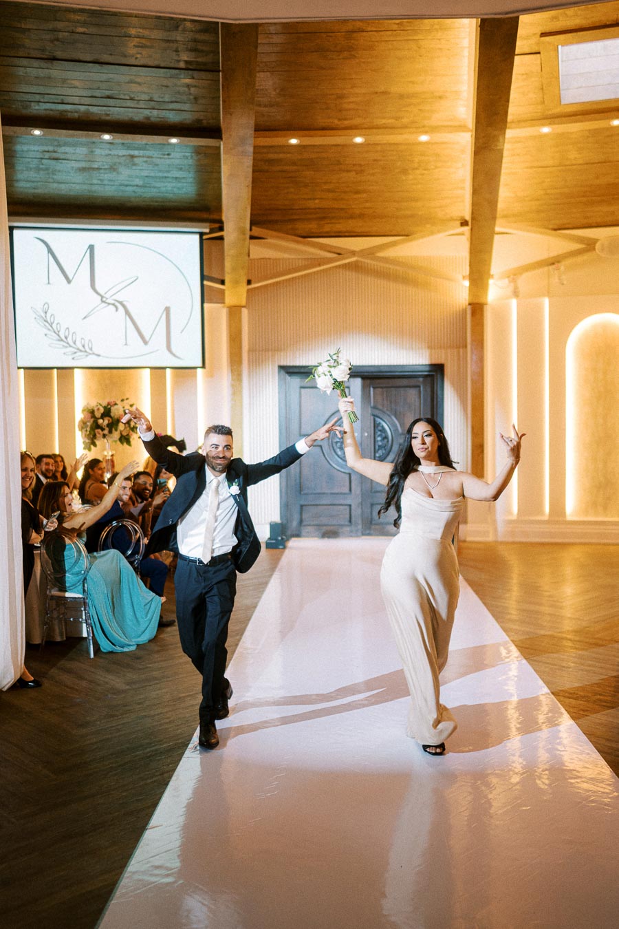 A joyful couple makes a grand entrance at their wedding reception, greeted by cheering guests in an elegantly decorated