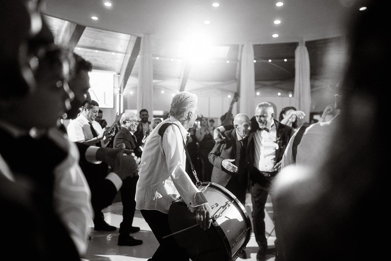 Black and white photo of a lively celebration with people dancing and a drummer in the foreground, capturing joyful