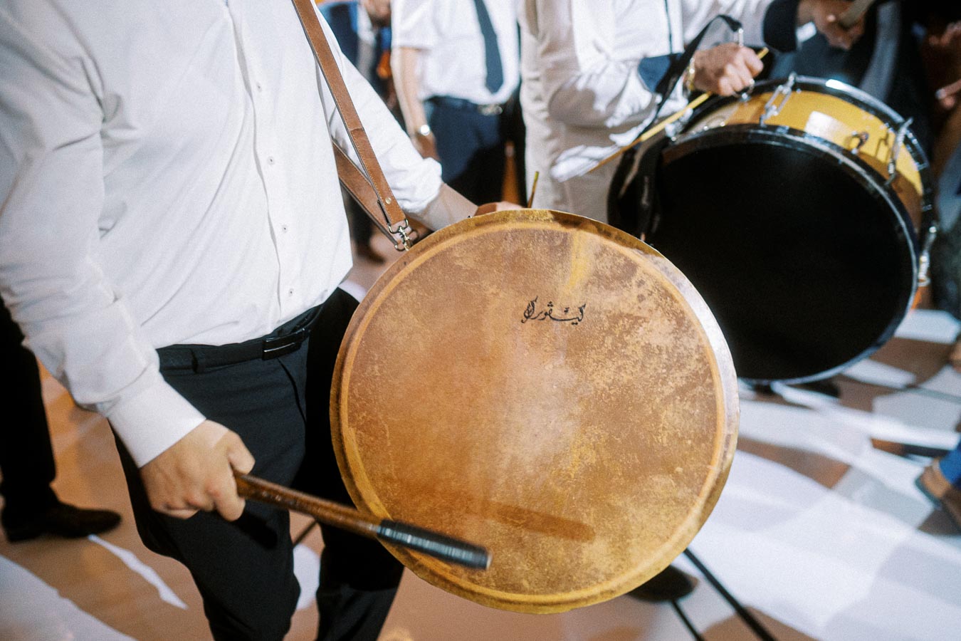 A musician wearing a white shirt plays a traditional drum at a lively event, capturing the energy and cultural ambiance.