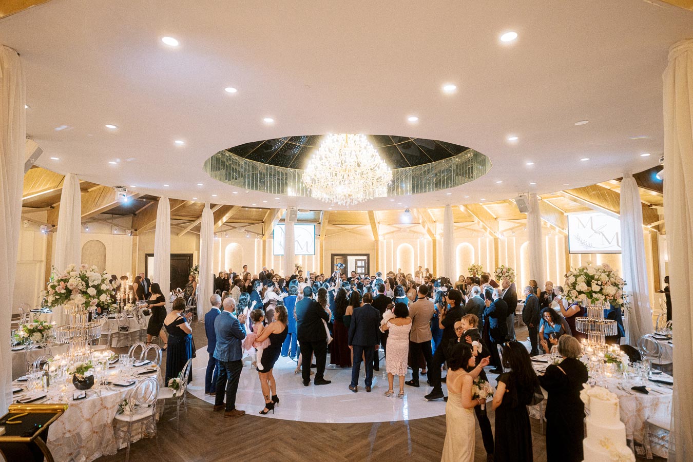 A vibrant wedding reception in an elegantly decorated banquet hall, featuring a large, illuminated chandelier hanging from