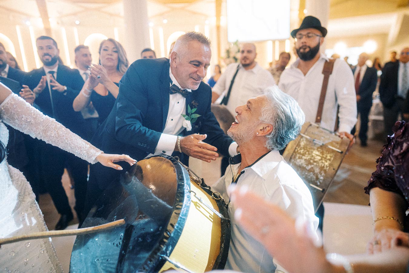 A lively wedding celebration with a joyful drummer interacting with the guests, elegantly dressed attendees clapping and