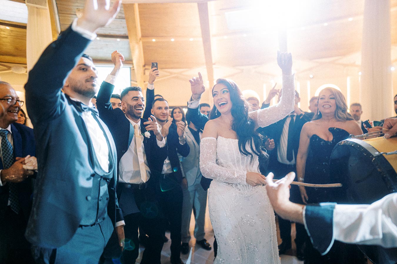 A joyful bride in a white wedding dress dances energetically with guests at a lively wedding reception, surrounded by