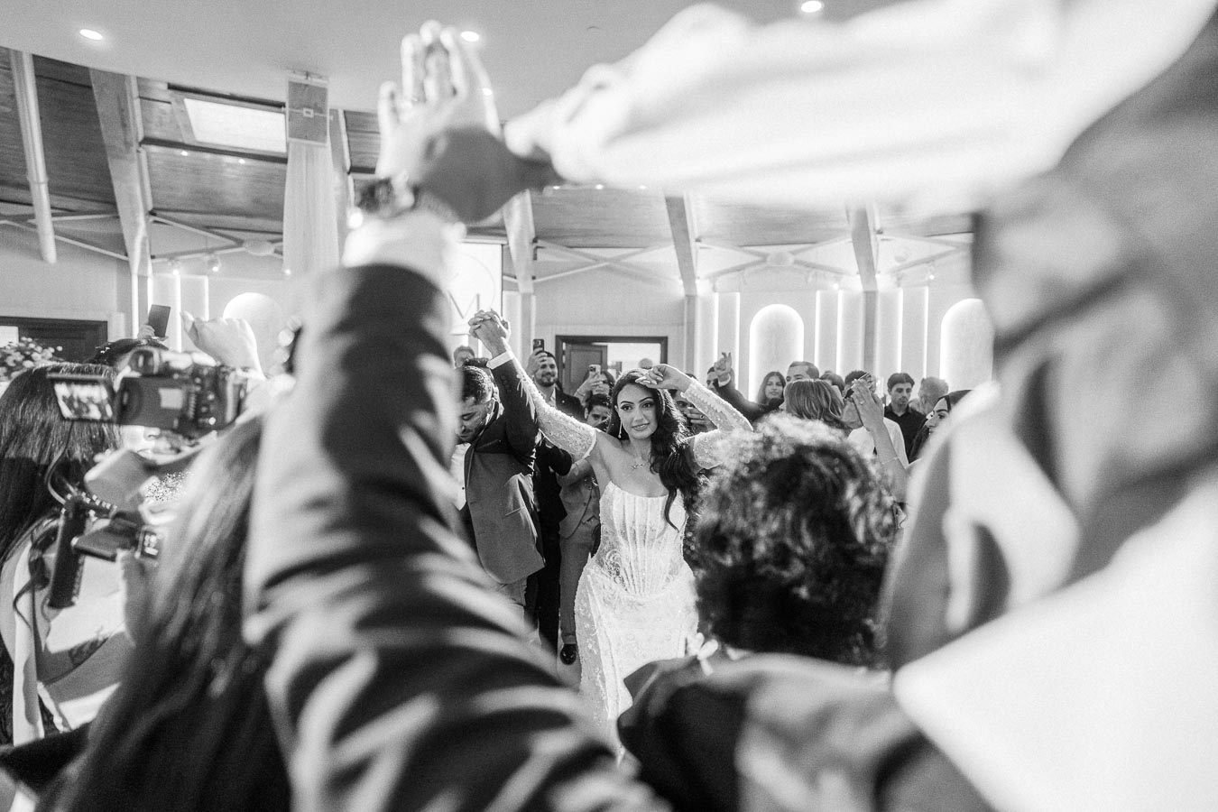 Black and white photo of a bride and groom dancing surrounded by guests at a wedding reception.
