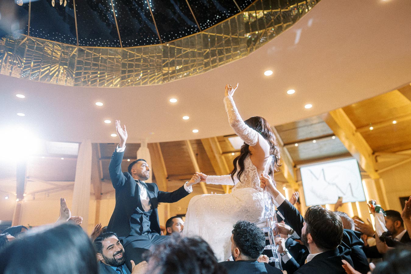 Joyous wedding celebration with bride and groom lifted on chairs during traditional dance at a glamorous reception venue