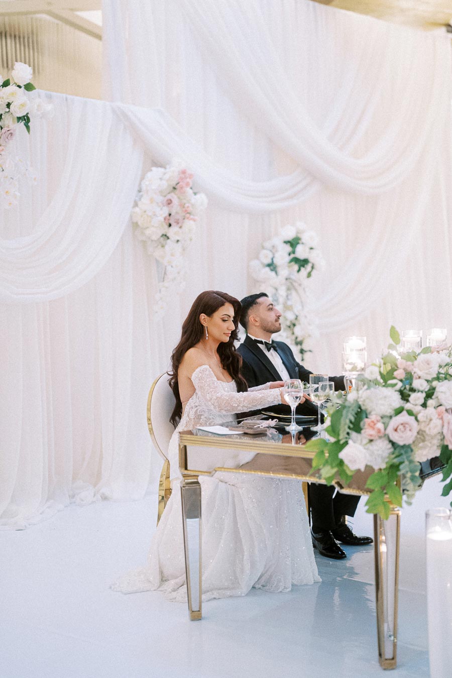 Elegant wedding reception with a bride in a lace gown and a groom in a tuxedo sitting at a beautifully decorated table,