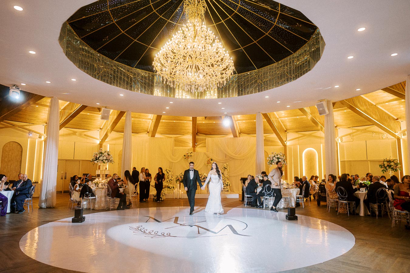 Elegant wedding reception in a luxurious venue with a grand chandelier and decorated tables. Bride and groom