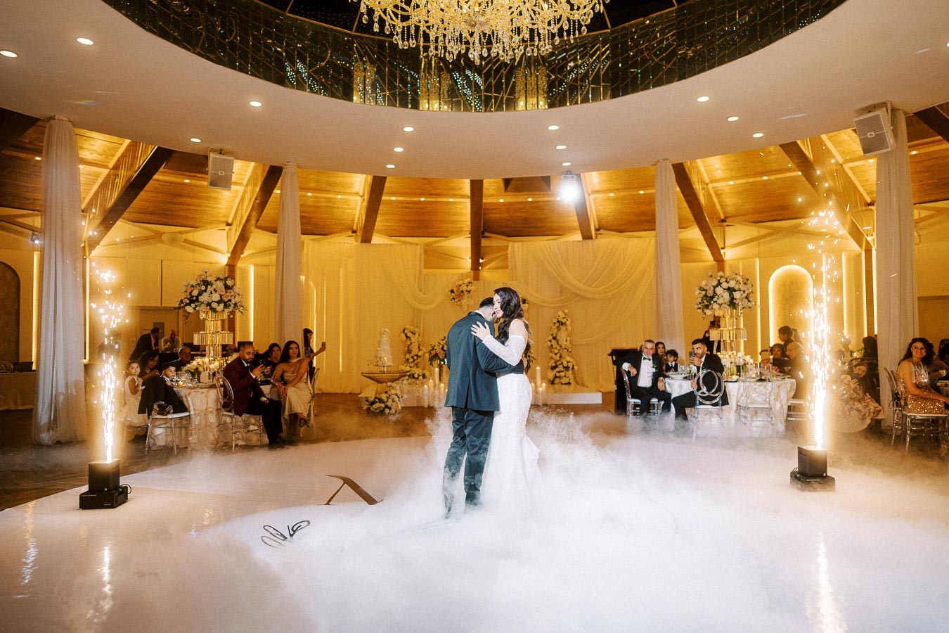 A bride and groom share their first dance in a beautifully decorated wedding venue, illuminated by ambient lighting and