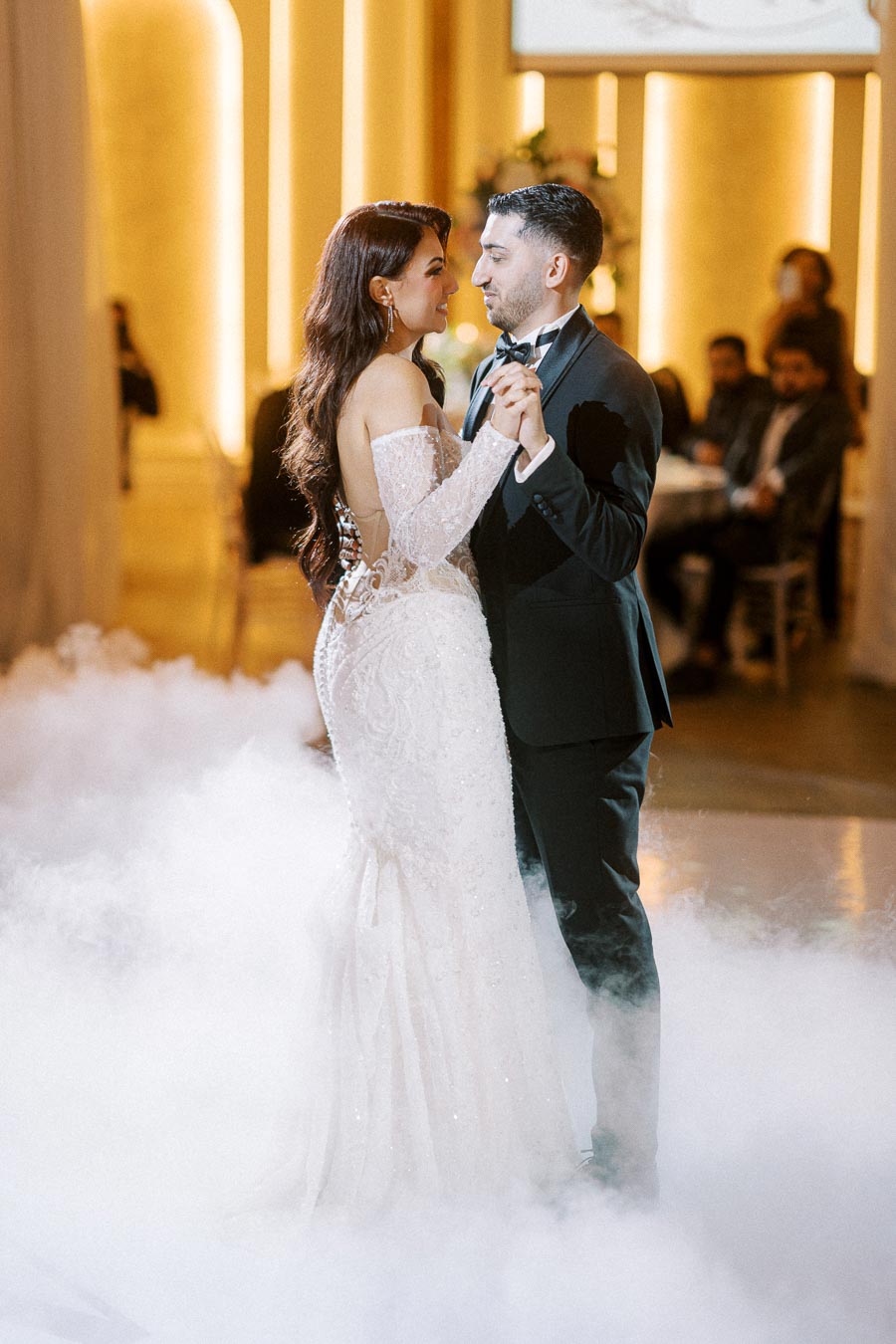 Couple sharing a romantic first dance at their elegant wedding reception, surrounded by mist and warm lighting.