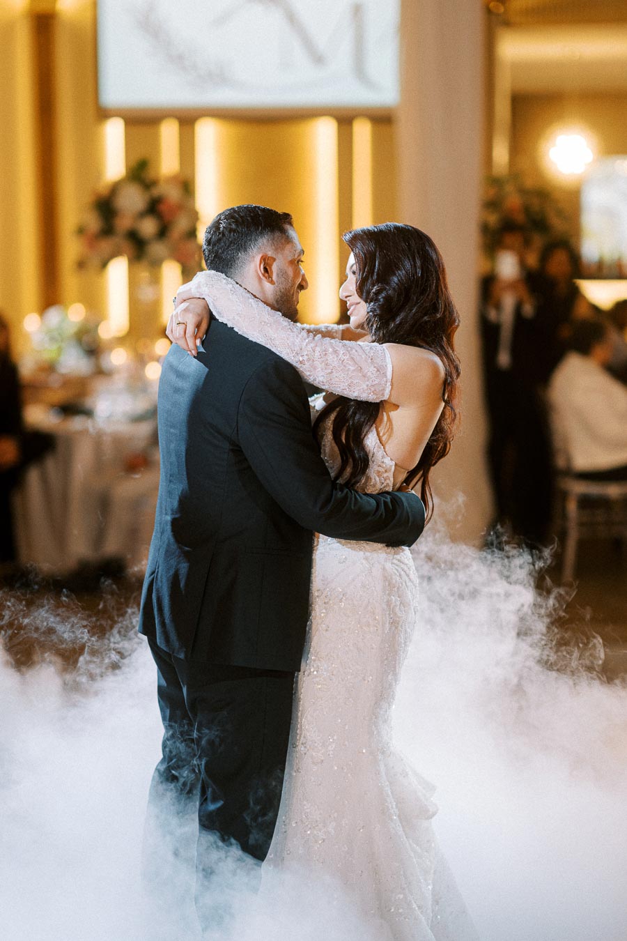 A bride and groom share a romantic first dance surrounded by elegant decor and soft mist at their wedding reception.