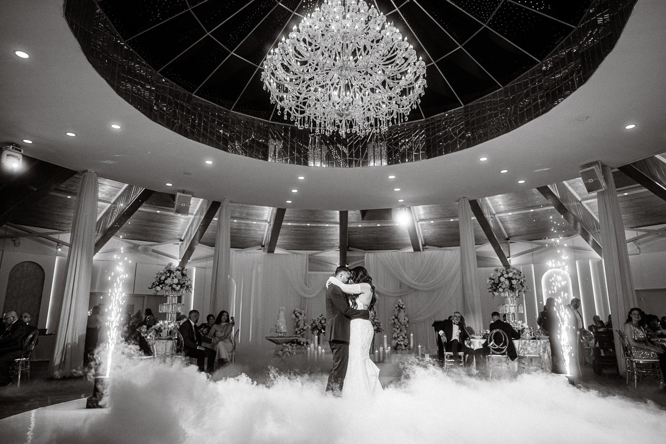 Elegant wedding couple sharing their first dance under a grand chandelier in a beautifully decorated venue, surrounded by