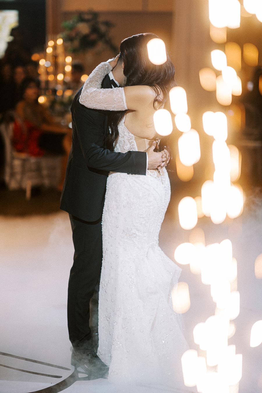 Romantic first dance of bride and groom in elegant ballroom setting, surrounded by soft lighting and warm ambiance.