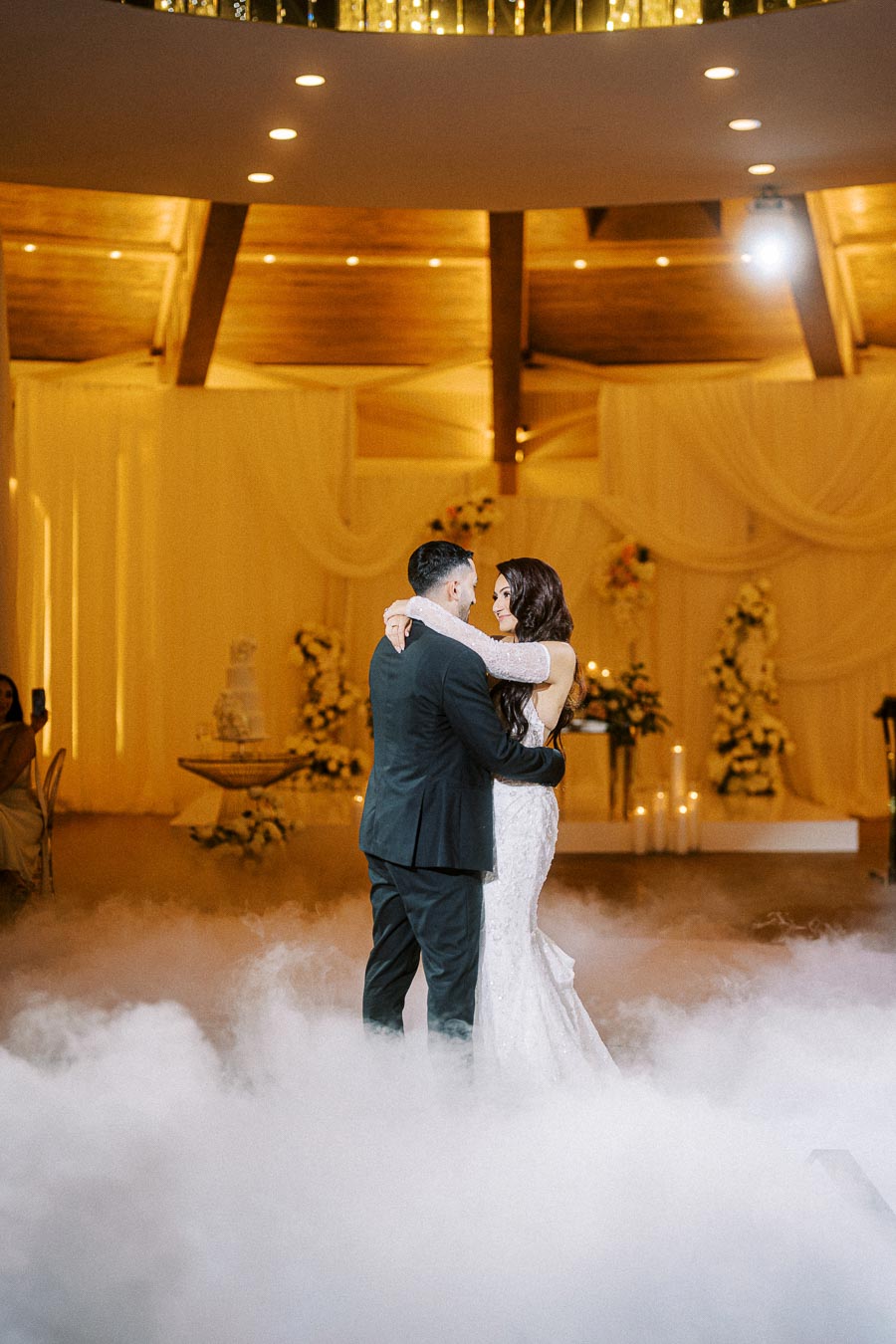 A bride and groom share their first dance surrounded by fog at a beautifully decorated wedding reception with a romantic