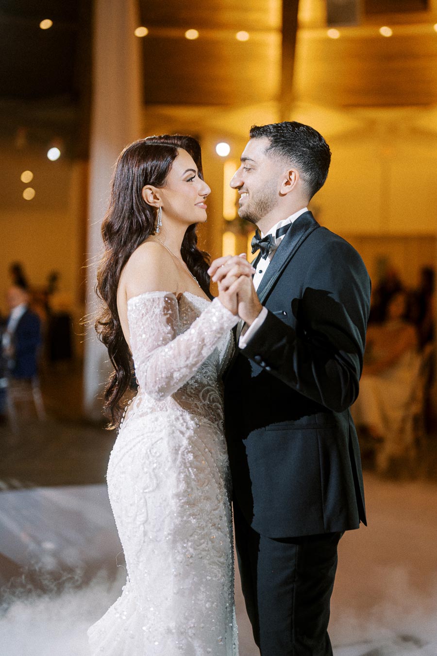 A bride and groom share their first dance at an elegant wedding reception, with the bride wearing a lace off-the-shoulder