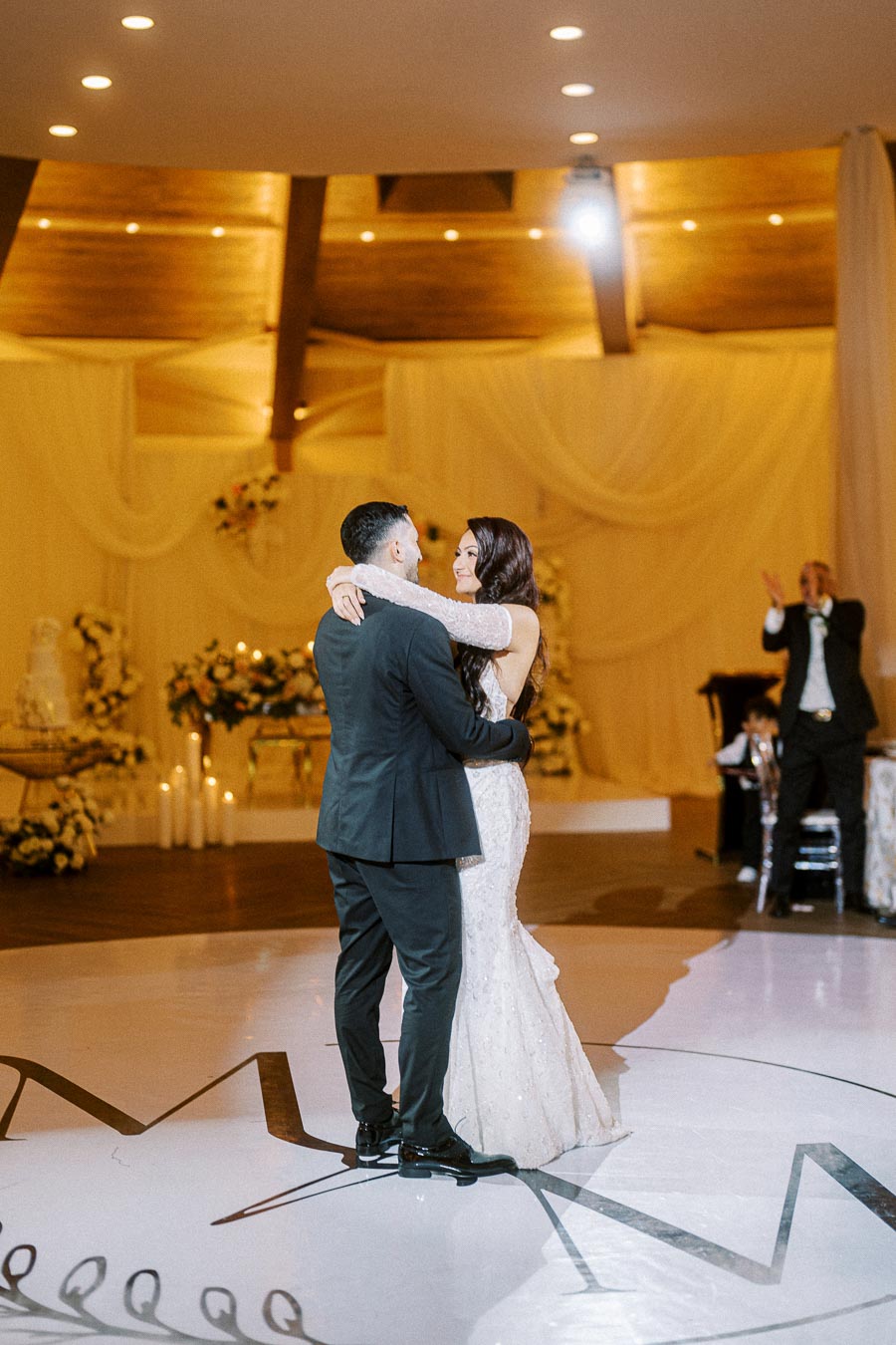 A newlywed couple shares their first dance at a beautifully decorated wedding venue, with dim lighting creating a romantic