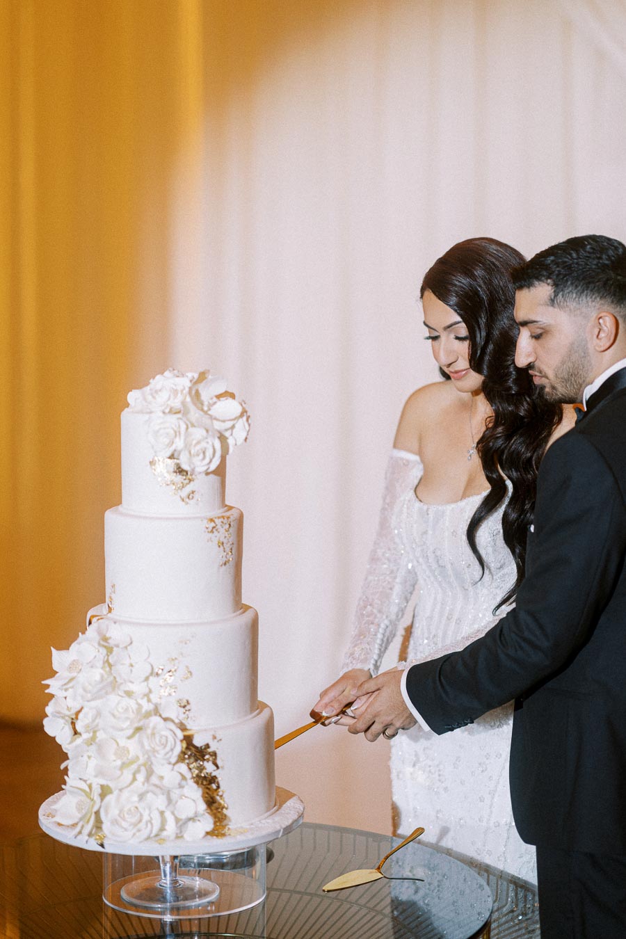 Couple cutting a four-tier white wedding cake adorned with floral decorations, symbolizing celebration and love at their
