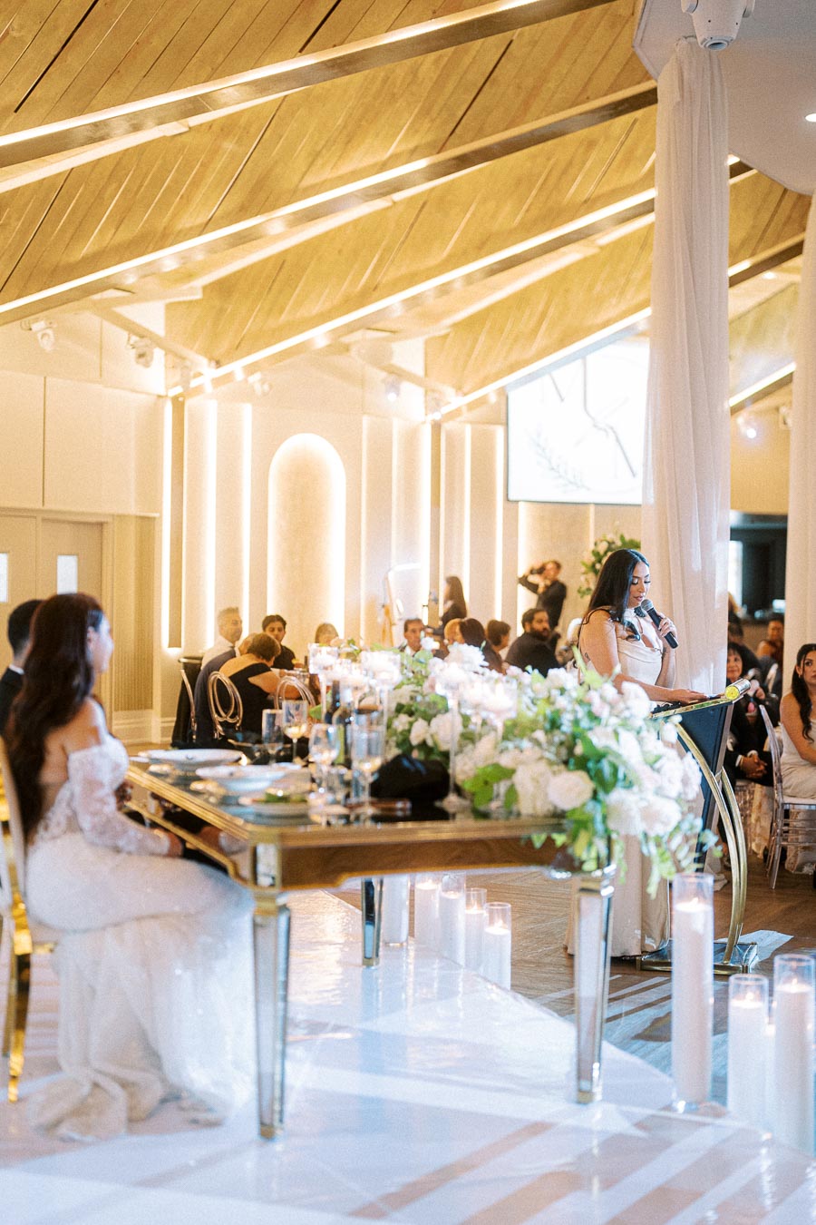 Elegant indoor wedding reception with a modern wooden ceiling, featuring a decorated table with white floral arrangements