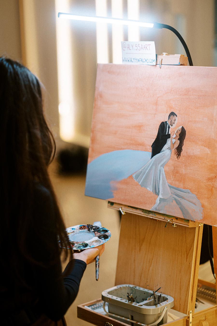 Artist painting a romantic wedding scene on a canvas, featuring a couple in elegant attire. The artist holds a palette and
