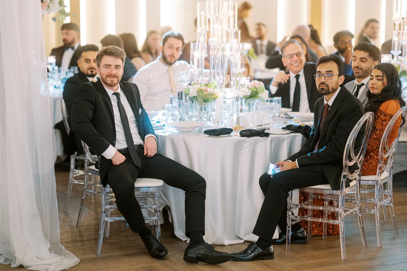 A group of well-dressed guests seated around an elegantly decorated table at a formal event, featuring floral arrangements